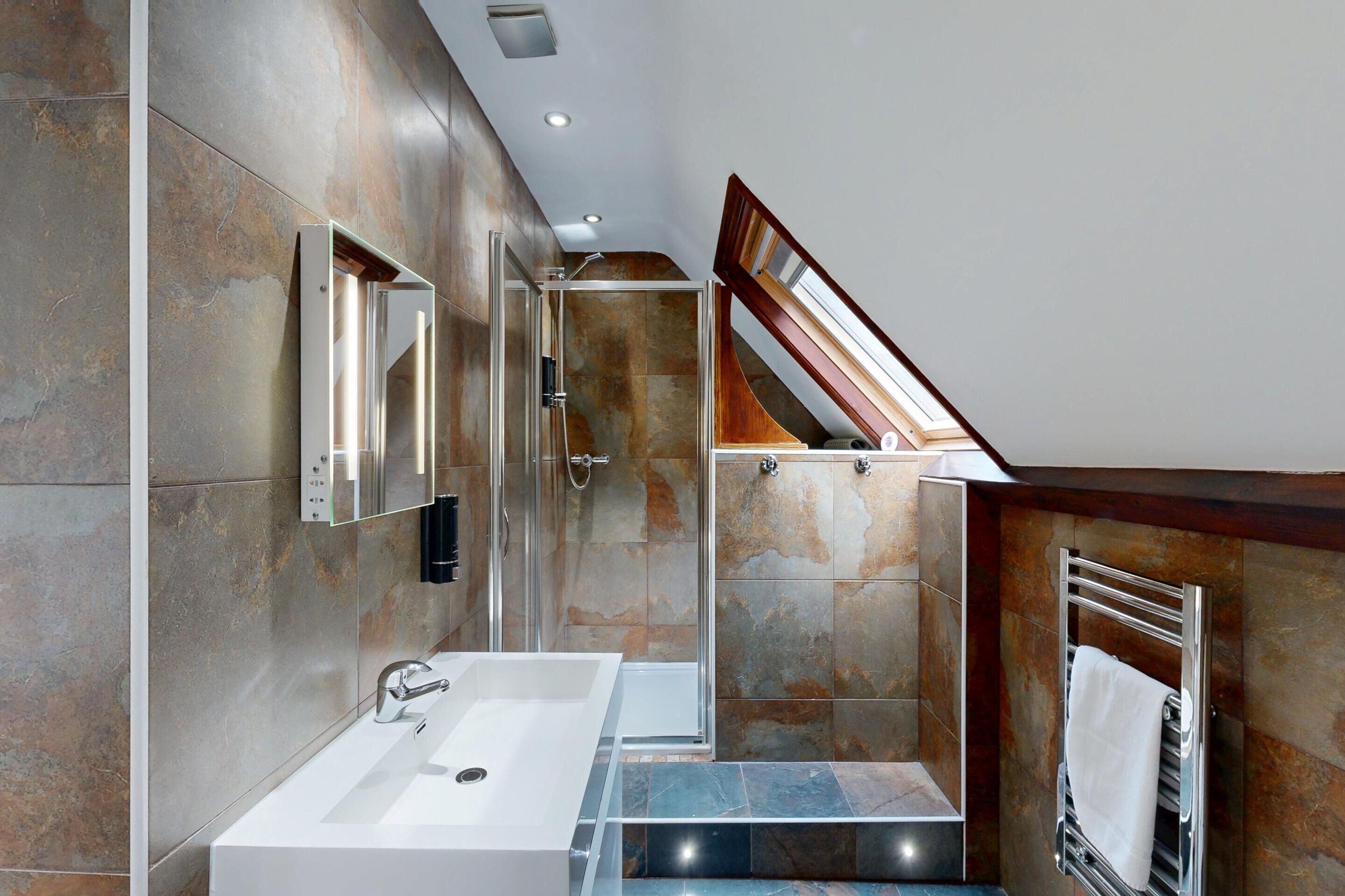 A modern bathroom with a large sink, a glass shower enclosure, and a wooden staircase leading to an upper level.