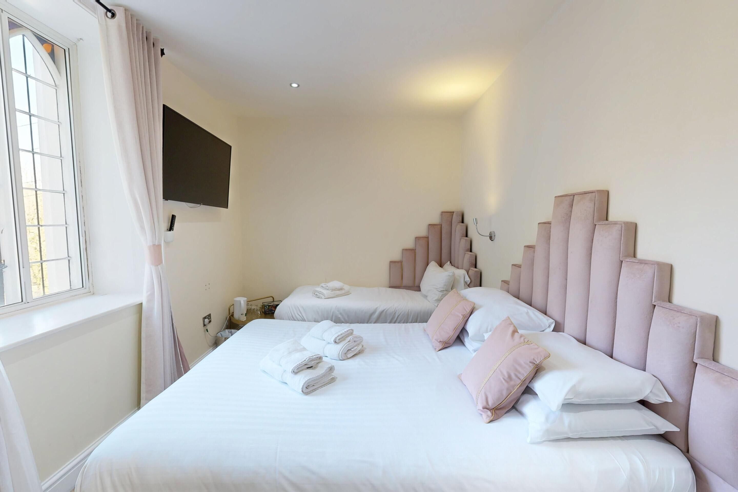 Une chambre d’hôtel avec deux lits, chacun doté d’une tête de lit, et une fenêtre avec des rideaux.