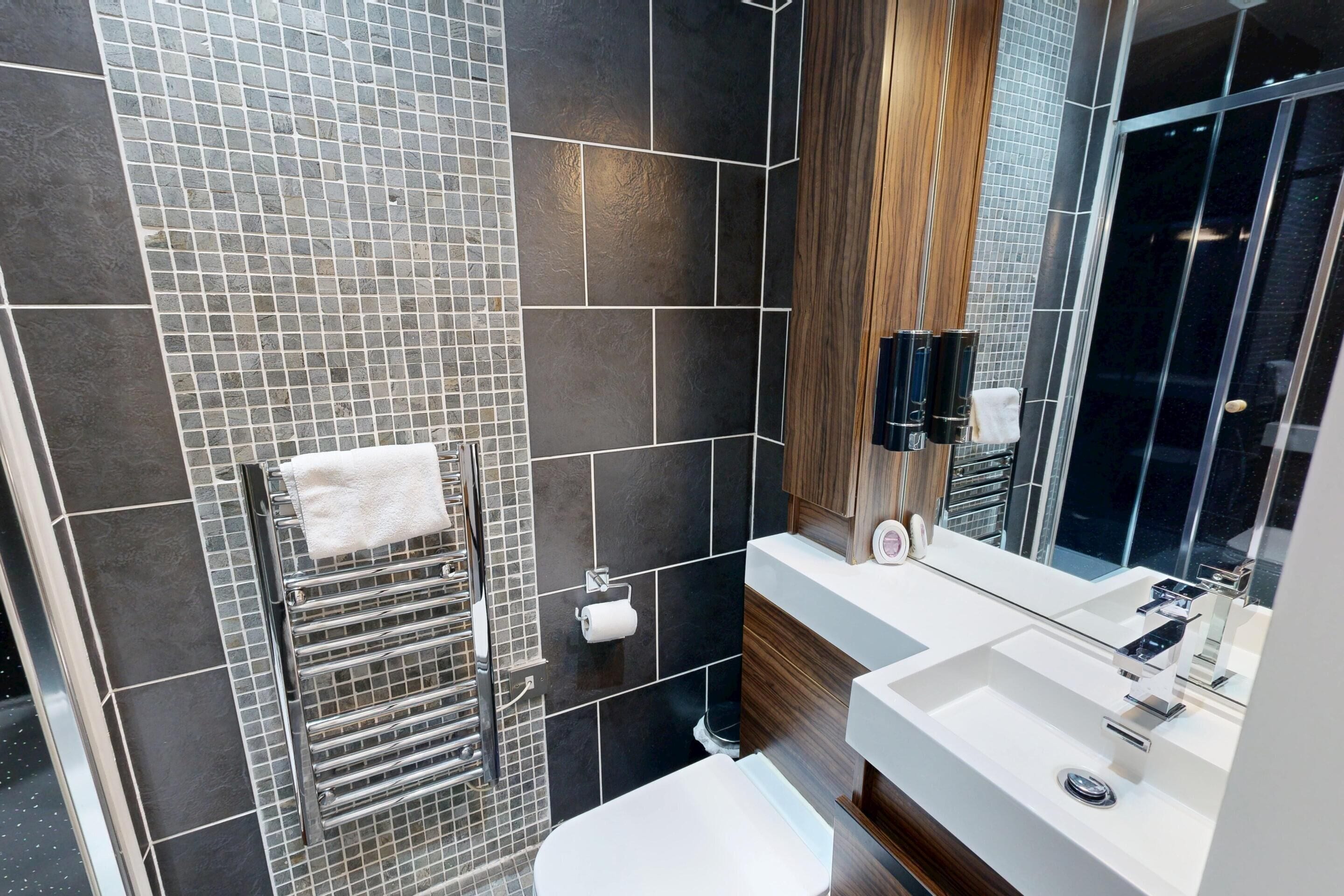 Un baño moderno con un espejo grande, un lavamanos blanco y un perchero para toallas.