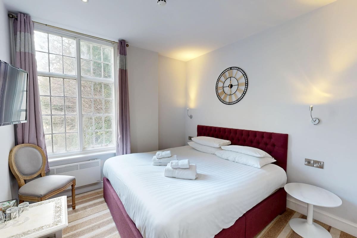 A hotel room with a large bed, a TV, a small round table, and a window with curtains.