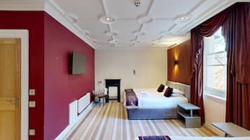 Quarto de hotel com uma cama grande, uma escrivaninha, lareira e janela com cortinas.