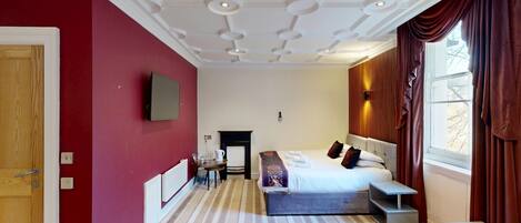 Una habitación de hotel con una cama grande, un escritorio, una chimenea y una ventana con cortinas.