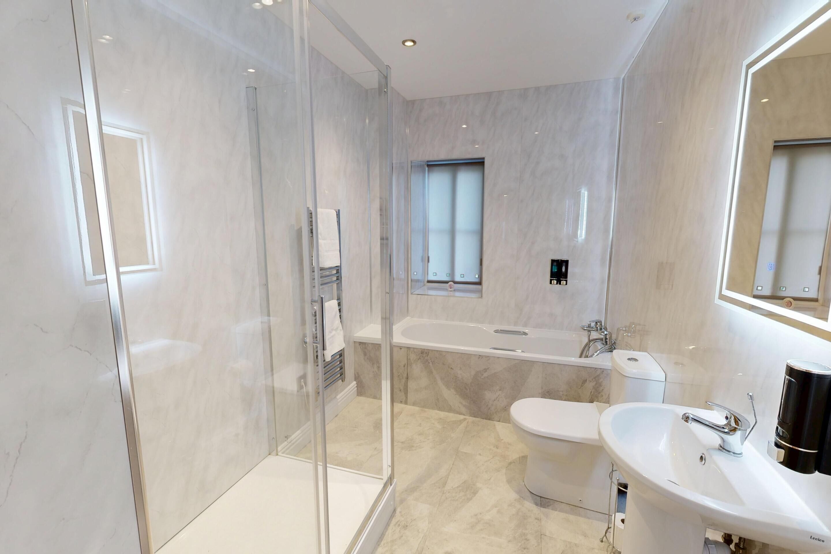 Un bany modern amb dutxa de vidre, banyera independent, vàter i un lavabo amb mirall a sobre.