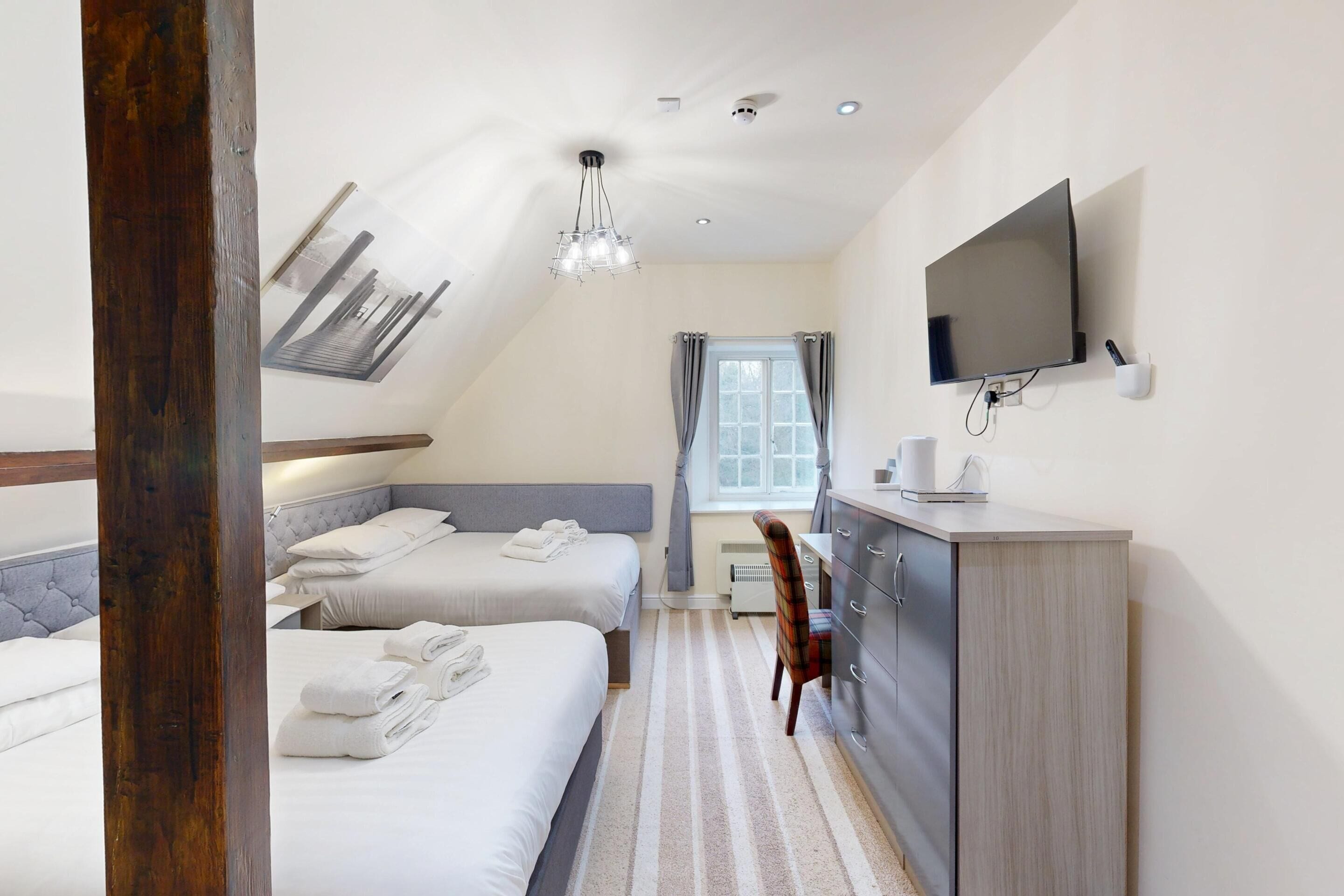Habitación de hotel con dos camas, un escritorio, una silla, un televisor y una ventana con cortinas.