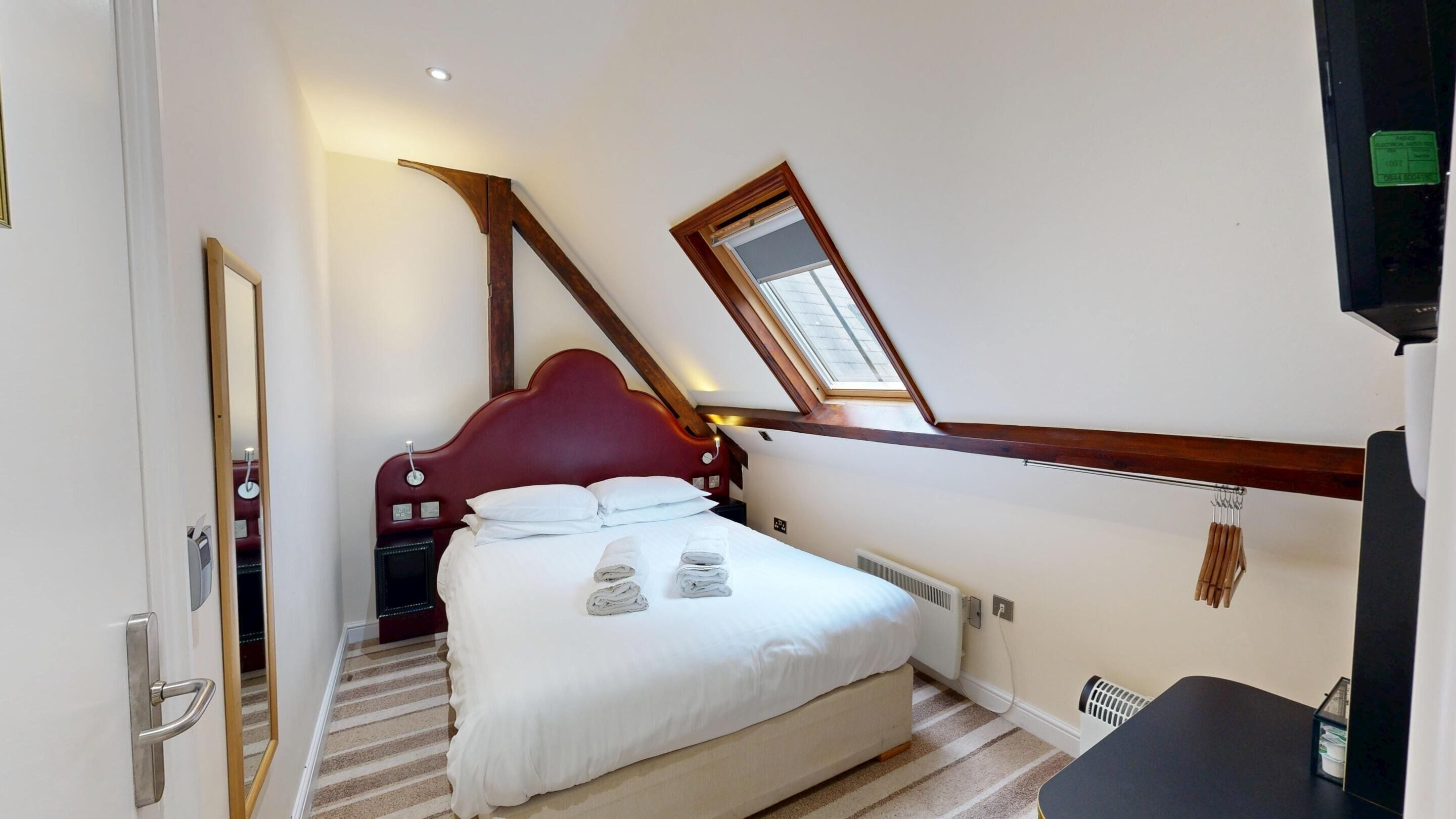 A bedroom with a large bed, a wooden headboard, a skylight, and a small desk.