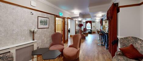A hotel lobby with a reception desk, seating area with chairs and sofas, a bar area, and a dining space.
