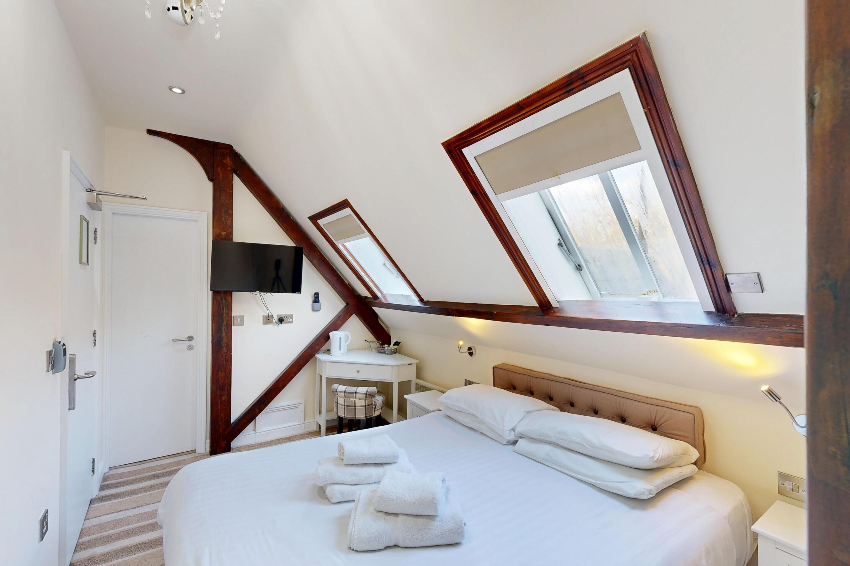 Ein Schlafzimmer mit einem großen Bett, einem Schreibtisch und einem Sessel. Ein Fenster bietet einen Blick ins Freie.