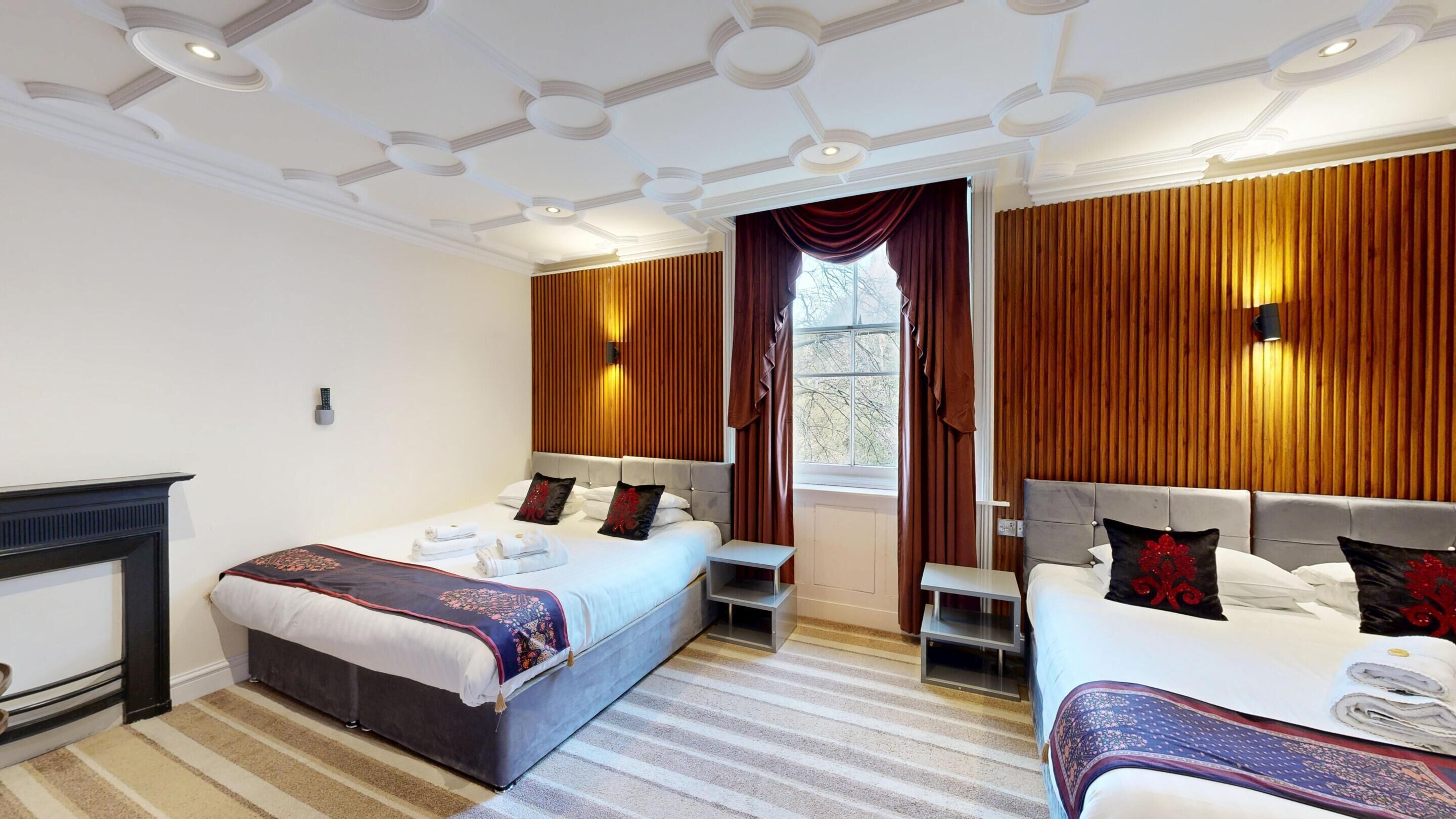A hotel room with two beds, a fireplace, and a large window with curtains.