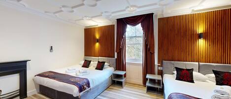 A hotel room with two beds, a fireplace, and a large window with curtains.