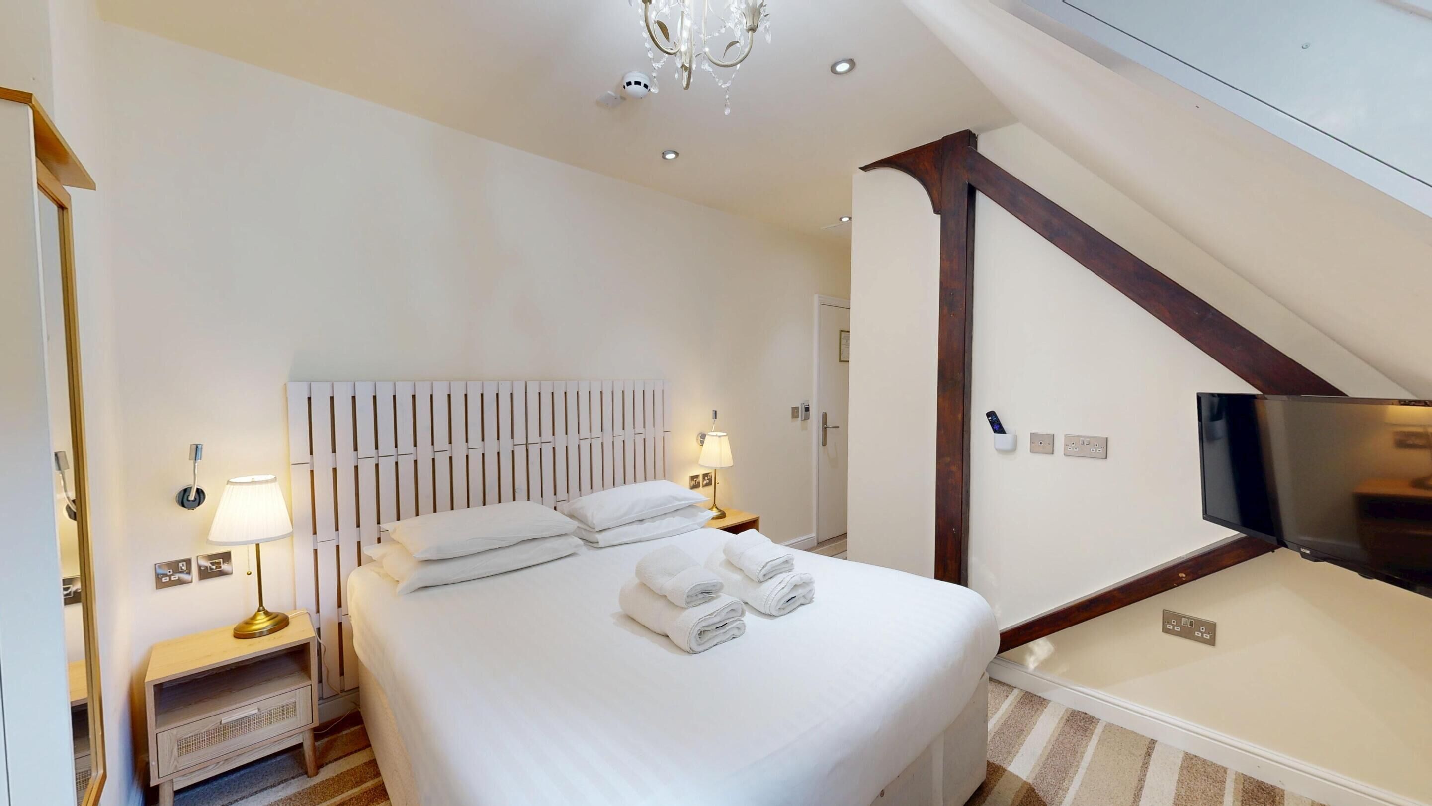 Una habitación de hotel con una cama bien hecha, lámparas de noche, un televisor de pantalla plana y una viga de techo de madera.