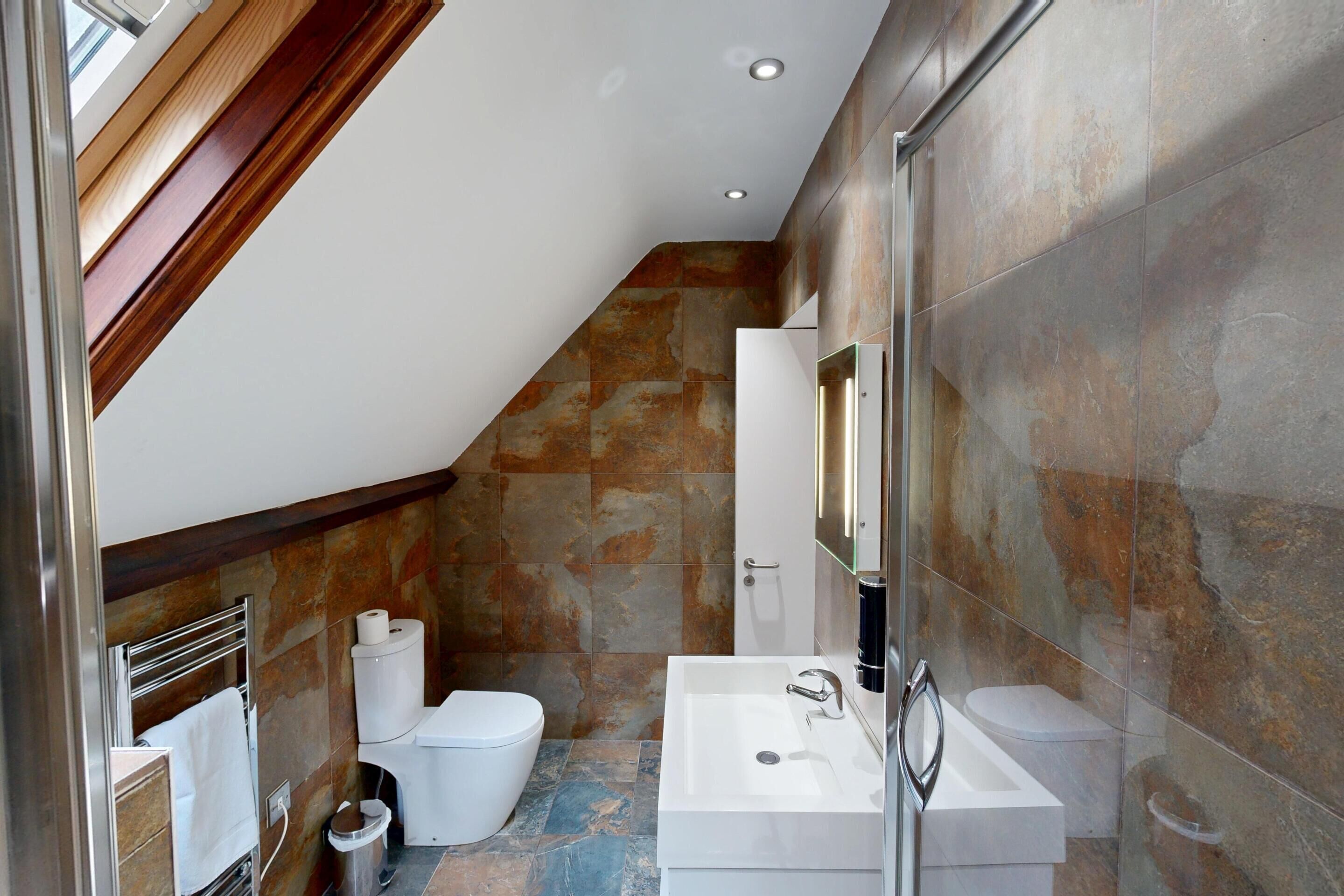 Un baño moderno con pared de piedra, un lavabo blanco y un inodoro.