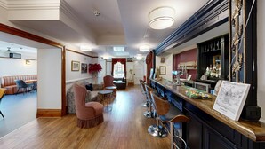 A bar area with a wooden counter, bar stools, and a bar stocked with bottles. There is a seating area with a sofa and chairs, and a dining area with tables and chairs. - High Tor Hotel (Matlock)