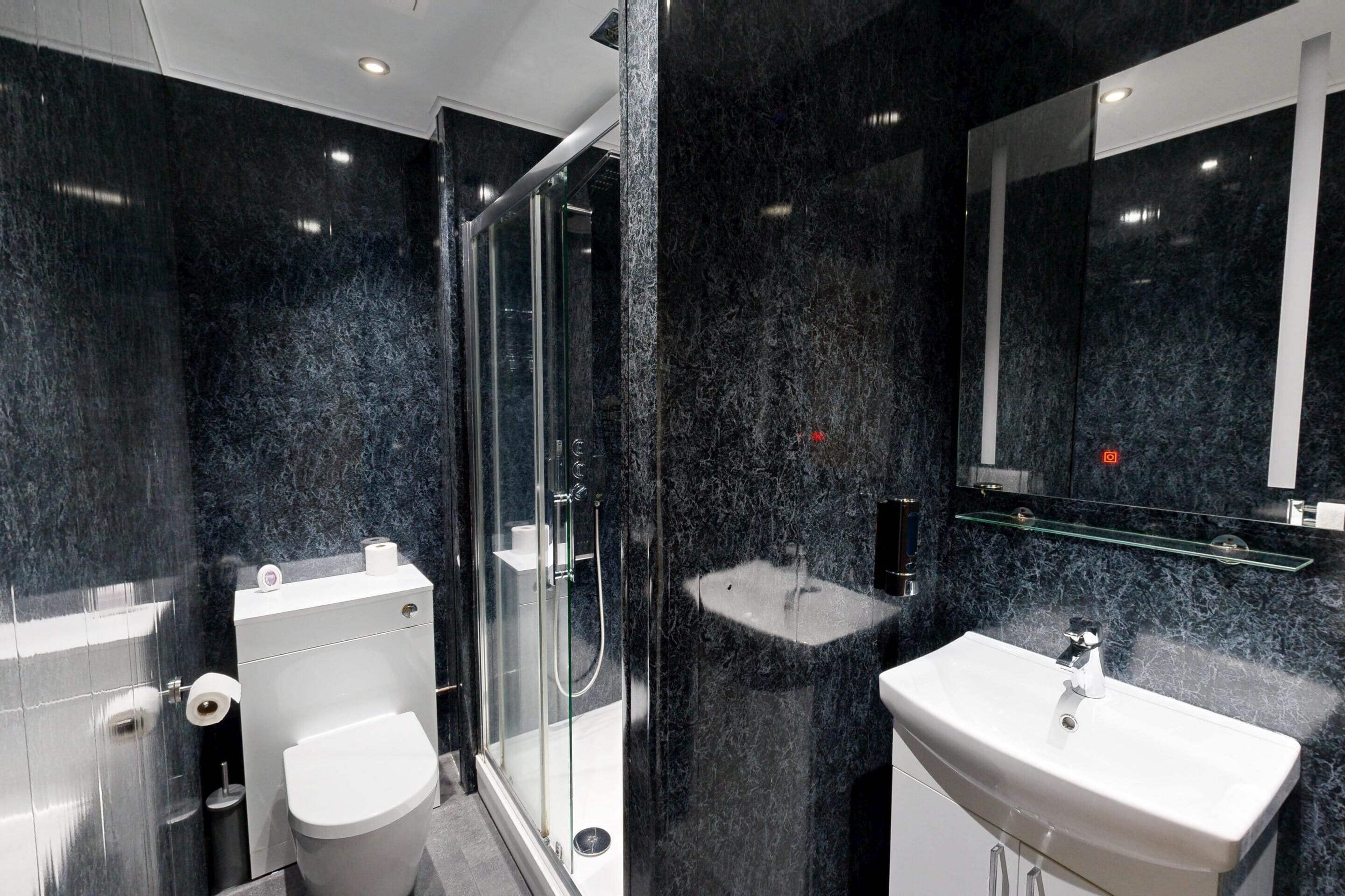 A modern bathroom with a glass-enclosed shower, a white toilet, and a white sink with a marble countertop.