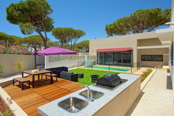 An outdoor kitchen area with a grill, sink, and wooden deck.