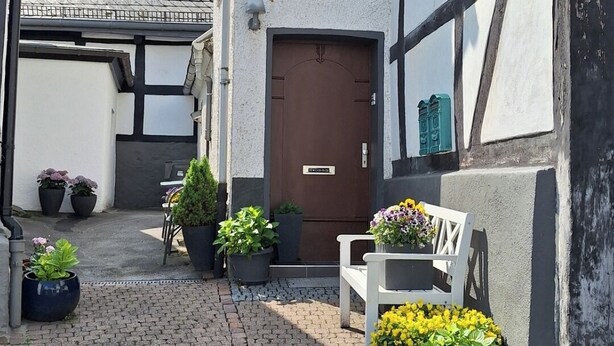 Ein Innenhof mit Kopfsteinpflaster, Blumentöpfen, einer Bank und einem Gebäude mit einer braunen Tür und einem kleinen Fenster.