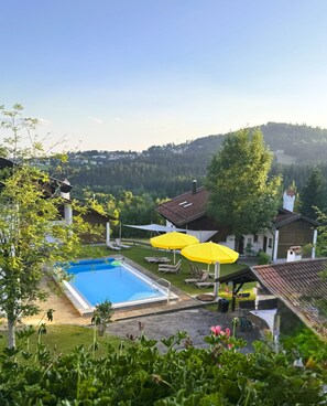 Une piscine bordée de parasols jaunes, de chaises longues, et offrant une vue sur une colline boisée.