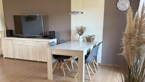 A modern dining area with a wooden table and chairs, a television on a cabinet, and a clock on the wall.