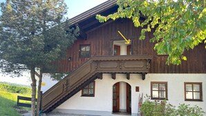 A two-story wooden house with a balcony, a staircase leading to the upper floor, and a small door on the ground floor.