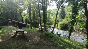 Una mesa de picnic en un área boscosa con un río y una cabaña al fondo.