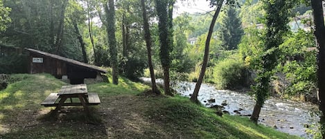 A picnic table in a wooded area with a river and a cabin in the background.