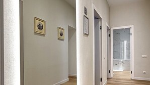 Un pasillo con suelo de madera, paredes blancas y un muro espejado en un lateral. Hay puertas que dan a otras habitaciones y dos cuadros enmarcados en la pared.