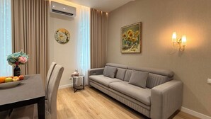 Una sala de estar moderna con un sofá gris, una mesa de comedor con frutas, un jarrón de flores y un cuadro en la pared.