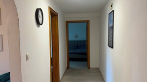 A hallway with a wooden floor, a clock on the wall, and a door leading to a bedroom. - Weserglück vacation apartment Grohnde (Emmerthal)
