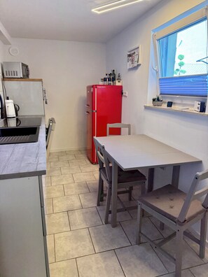 A compact kitchen with a dining table, chairs, a red refrigerator, and a window with blinds. - Weserglück vacation apartment Grohnde (Emmerthal)
