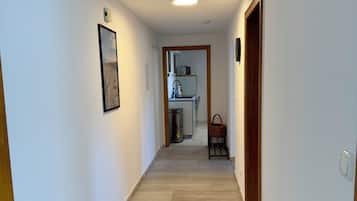A hallway with a wooden floor, a framed picture on the left wall, and a kitchen area visible through an open doorway.
