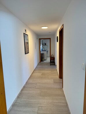 A hallway with a wooden floor, a framed picture on the left wall, and a kitchen area visible through an open doorway. - Weserglück Vacation Apartment in Grohnde (Emmerthal)