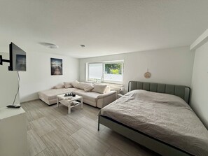 A modern bedroom with a bed, a sofa, a coffee table, and a TV. - Weserglück Vacation Apartment in Grohnde (Emmerthal)