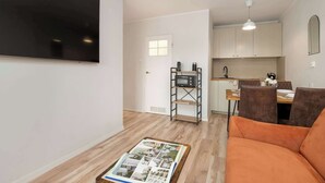 Un apartamento moderno con televisor de pantalla plana, una zona de comedor con mesa y sillas, una cocina con armarios y un sofá.