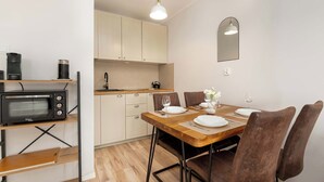 Una cocina compacta con microondas, hervidor de agua y una mesa de comedor de madera preparada para cuatro comensales.