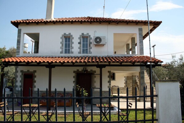 A two-story house with a tiled roof, a balcony, and a fenced front yard. - Villa Halkidiki - Nea Kalikrateia - 2-bedroom Apartment (Nea Propontida)