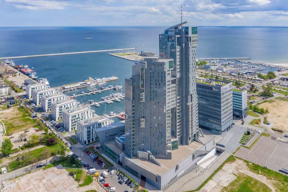 Un edificio de gran altura con un diseño arquitectónico moderno, situado cerca de un puerto deportivo con barcos amarrados.