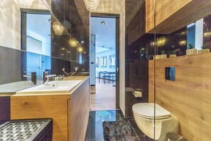 A modern bathroom with a wooden vanity, a glass shower enclosure, and a visible toilet. - Elegant Apartment with Sea View | Parking (Gdynia)