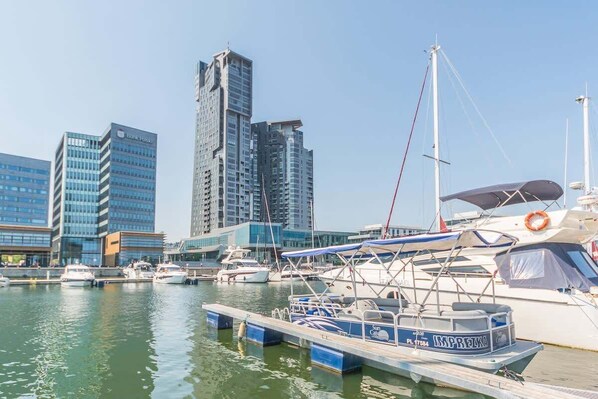 A marina with boats docked, a tall building with a modern design, and a clear sky.