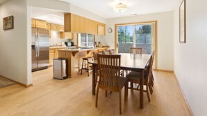 A modern kitchen with wooden cabinets, a stainless steel refrigerator, and a dining area with a wooden table and chairs. - 6 Approach 4 Bedroom Home (Bend)