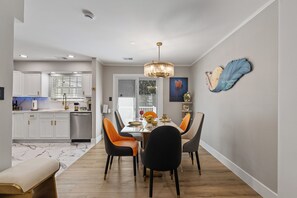A modern kitchen with white cabinets, a dining area with a marble floor, and a chandelier.
