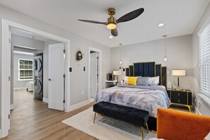 A bedroom with a bed, a bench, a nightstand, a ceiling fan, and a window with blinds.