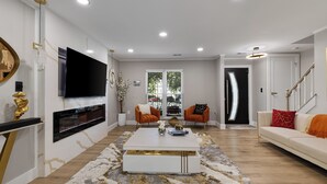 Una sala moderna con televisor de pantalla plana montado en la pared, un sofá blanco, dos sillones, una mesa de centro y una escalera que lleva a otro nivel.