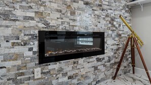 Una chimenea moderna con un muro de mosaico de piedra, un televisor montado y un trípode.