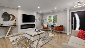 Een moderne woonkamer met een flatscreen-tv, een open haard, een witte salontafel en twee oranje fauteuils.