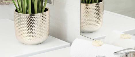 A bathroom with a white sink, a mirror, and two potted plants with green foliage.