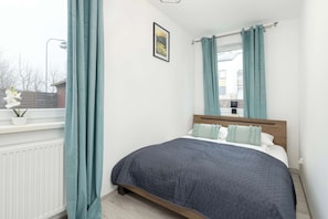 Quarto com cama, janela com cortinas, radiador e uma pequena planta em vaso.