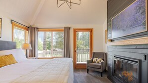 A hotel room with a bed, a chair, a fireplace, and large windows. - 7 Vine Maple 4 Bedroom Home (Bend)