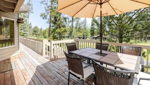 A wooden deck with a table and chairs, an umbrella, and a view of trees. - 7 Vine Maple 4 Bedroom Home (Bend)