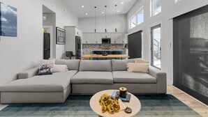 Una sala moderna con un sofá seccional gris, una mesa de centro y una cocina al fondo.