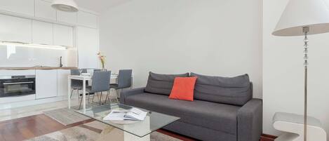 Una sala moderna con un sofá gris, una mesa de centro de vidrio y una lámpara blanca.