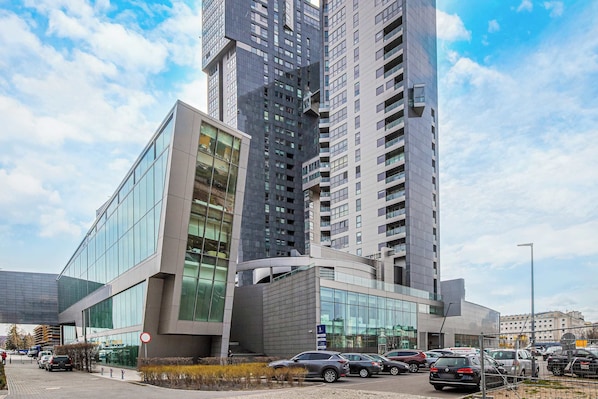 A modern building with large glass windows and a parking lot with several cars.